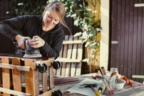 Kvinna som malar en självgjord rack utomhusbyggnad från palle - upcycling