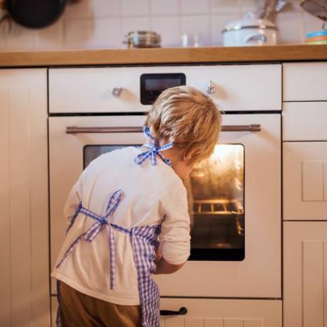 Liten pojke som inomhus ser ugnen som bakar