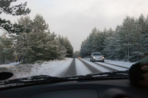 En bil kör på vägen täckt av snö bland träd