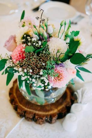 Bröllop tabell blomma dekoration. Glasvas med bordnummer för gäster med grönska, rosor, lisianthus och andra blommor.