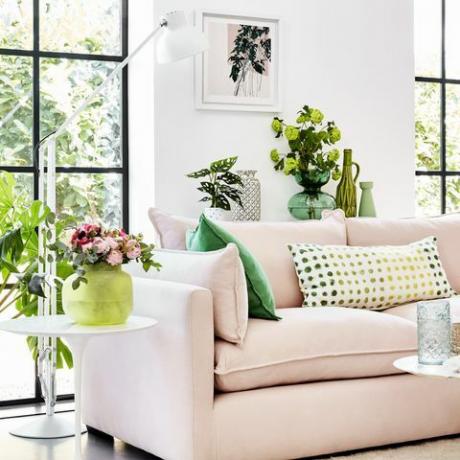 rosa soffa i ett vitt rum med gröna växter runt och gröna mönstrade kuddar