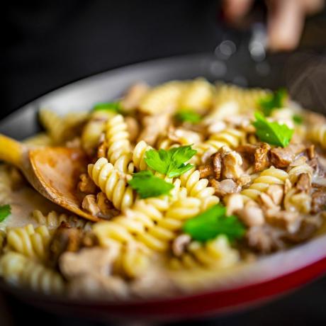 kvinna hand lagar välsmakande kycklingfilé med svamp i en krämig sås med fusilli pasta i pannan på köket