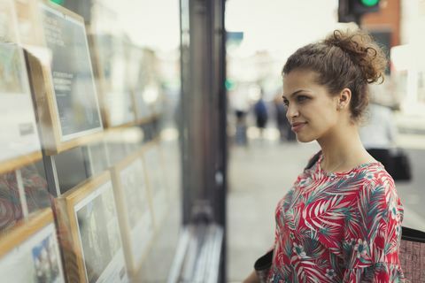 Ung kvinna som bläddrar i fastighetslistor på stads- butik