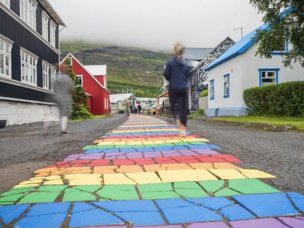 Island, Seydisfjordur, människor som går längs den regnbågsfärgade asfaltvägen mitt i en avskild stad