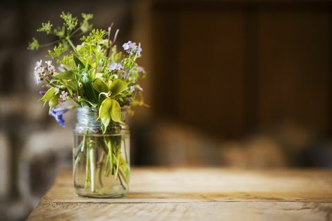 Stäng sig upp av en glasburk med en liten grupp vilda blommor på ett trätabell.