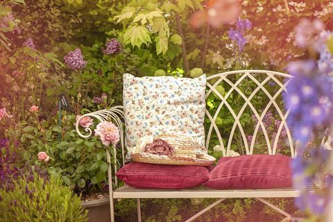 En vacker trädgårdsstol i sommargjutning med kuddar och en sommarhatt, sjaskig chic scen